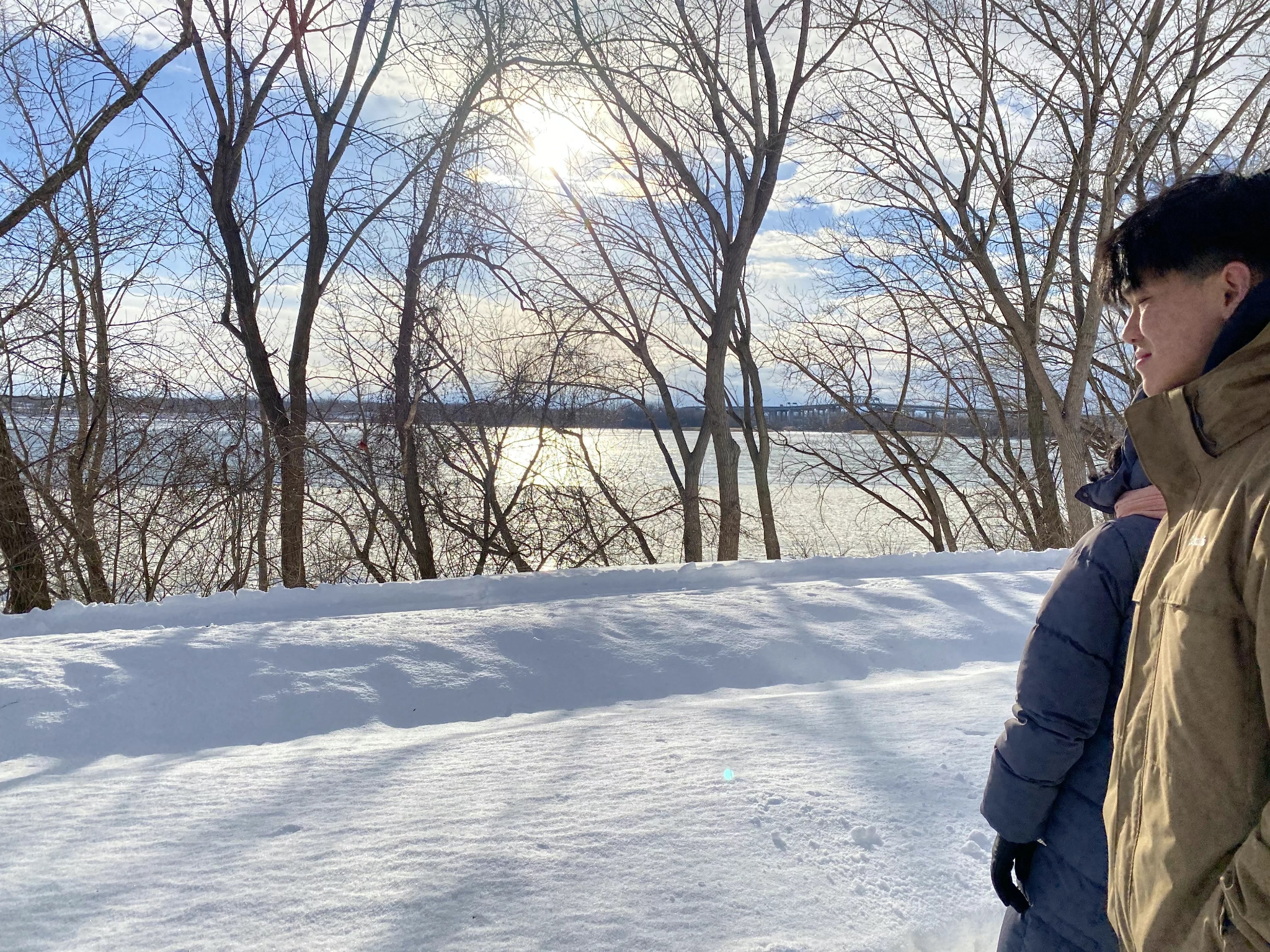 积雪河岸、落叶树木、河面日光、远桥与路旁的人。